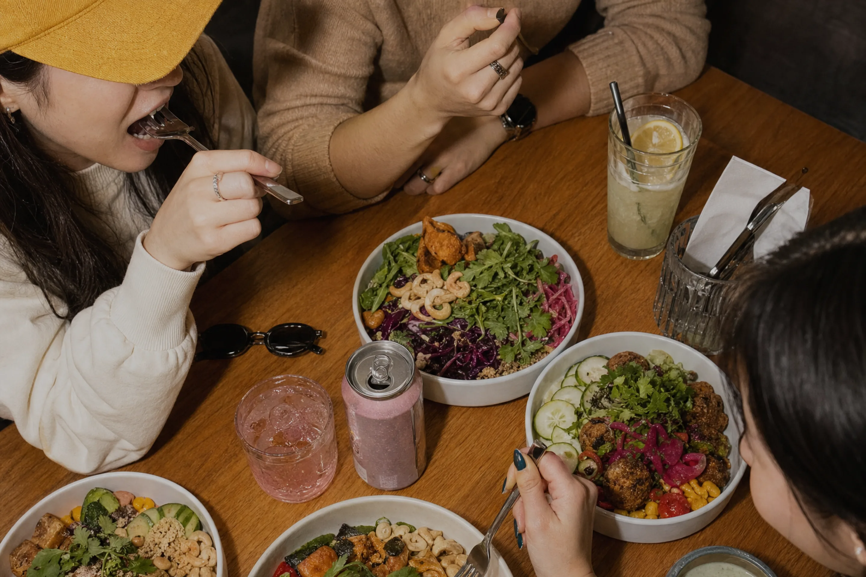 Friends sharing bowls of salad and grain dishes around a wooden table